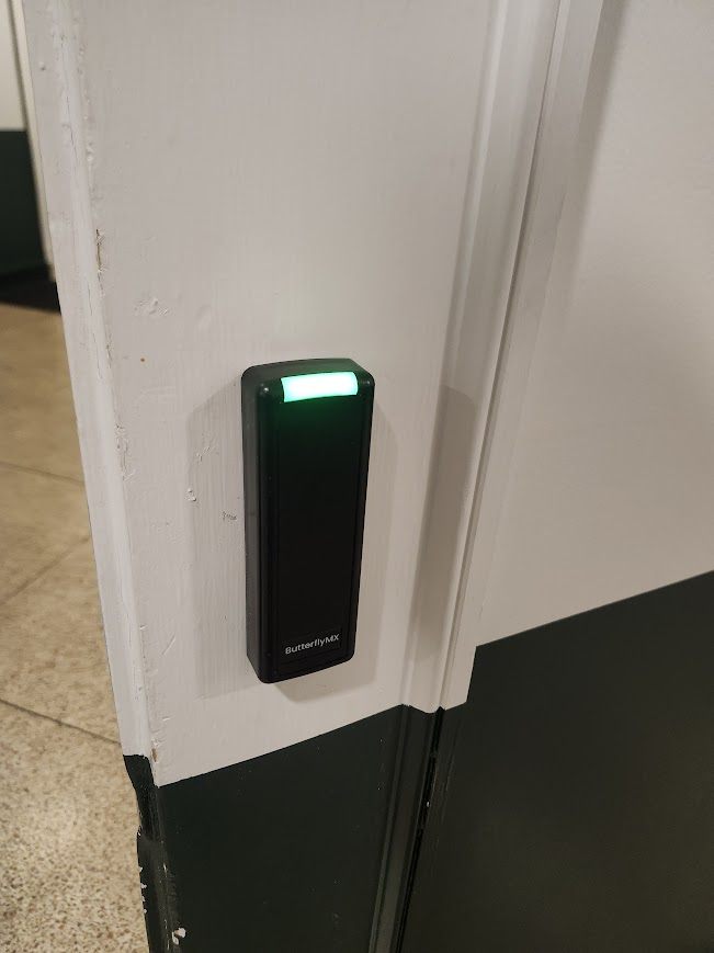 Black access control reader with a green status light mounted beside a doorway
